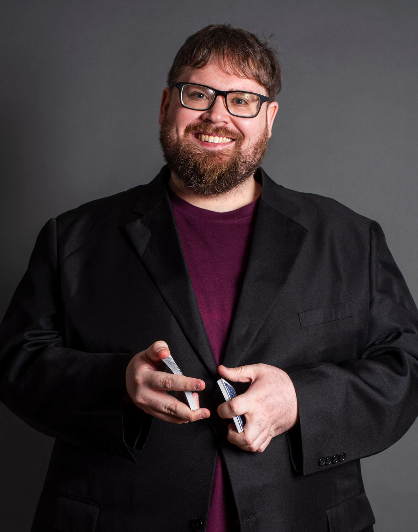 Dan wearing a black blazer over a red shirt about to shuffle a deck of cards.
