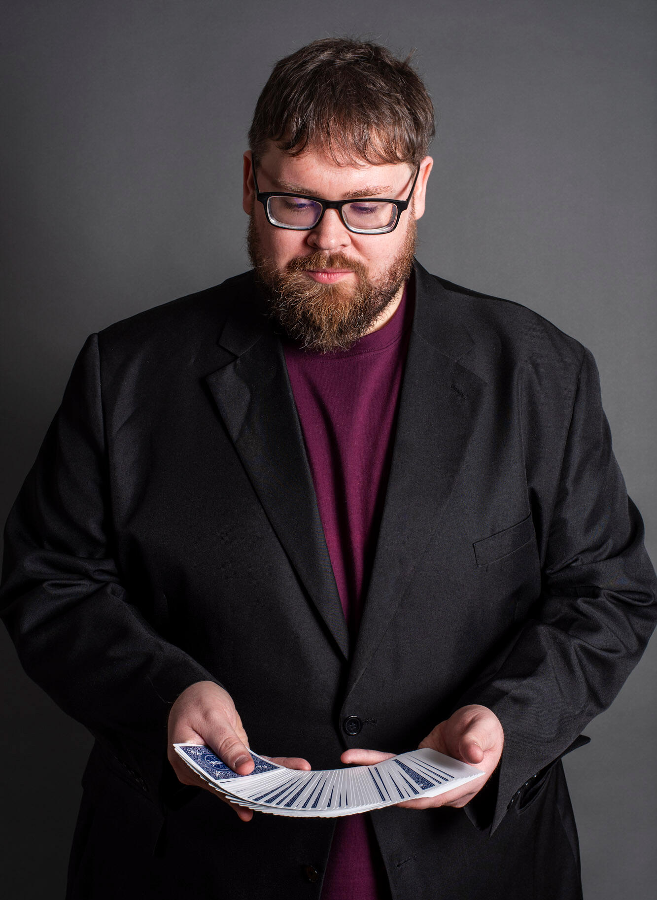 Dan Feltey Dan wearing a black blazer over a red shirt spreading a blue deck of cards.